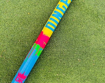May include: A colorful sports stick with a blue shaft, a yellow tip, and a pink and green section. The stick has the word "DINNER" in blue letters on the yellow tip and a crown logo with "DK" on the shaft.