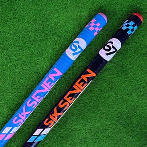 May include: Two hockey sticks with the text "SIX SEVEN". One stick is blue with pink and white accents, the other is black with orange and white accents. Both sticks have a checkered pattern at the top.