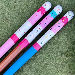May include: Three hockey sticks with ice cream cone designs. The sticks have pink, brown, and blue handles. The tops are white with pink, blue, and green sprinkles. The ice cream cone design is pink, blue, and brown.