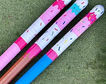 May include: Three hockey sticks with ice cream cone designs. The sticks have pink, brown, and blue handles. The tops are white with pink, blue, and green sprinkles. The ice cream cone design is pink, blue, and brown.