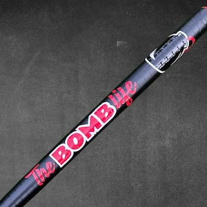 May include: A black and red baseball bat with the words "The BOMB life" in red and white lettering. The bat has a red grip and a black barrel. The bat is angled diagonally against a dark gray background.