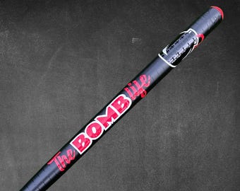 May include: A black and red baseball bat with the words "The BOMB life" in red and white lettering. The bat has a red grip and a black barrel. The bat is angled diagonally against a dark gray background.