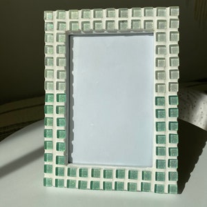 Könnte beinhalten: Ein weißer Bilderrahmen mit einem grün-weißen Mosaikrand. Der Rahmen besteht aus Keramikfliesen und hat eine glänzende Oberfläche.