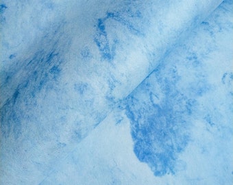 May include: A close-up of a light blue fabric with a marbled pattern. The fabric is folded in half, creating a diagonal line across the image.