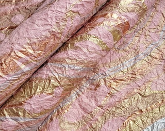 May include: Close-up of a crumpled pink and gold metallic wrapping paper. The paper has a textured, crinkled surface with a metallic sheen.