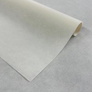 May include: A roll of off-white, translucent parchment paper. The paper is partially unrolled, revealing a soft, textured surface. The rolled portion shows a cylindrical shape. The background is a light grey, textured surface.