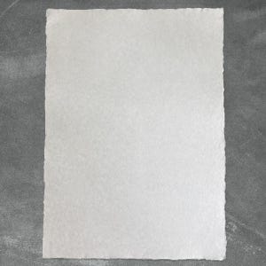 Puede incluir: Una hoja rectangular de papel blanco con una superficie texturizada y bordes irregulares. El papel est&aacute; centrado sobre un fondo gris, creando un contraste. Los bordes del papel son desiguales, a&ntilde;adiendo una cualidad artesanal.