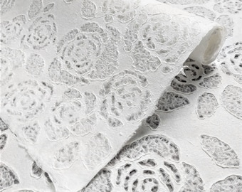 May include: White textured paper with a repeating pattern of embossed roses. The paper is rolled up and the edges are visible.