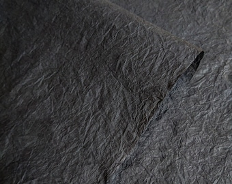 May include: A close-up of black textured paper. The paper has a crinkled, wrinkled, or crumpled appearance.