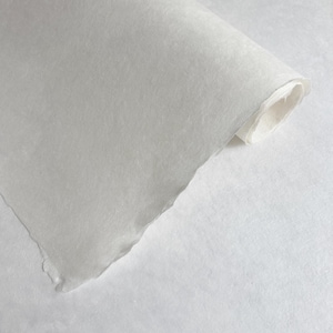 Könnte beinhalten: Eine Rolle cremefarbenes, strukturiertes Papier mit zerrissenem Rand. Das Papier ist teilweise abgerollt und zeigt einen gerollten Abschnitt. Die Oberfläche wirkt weich und leicht durchscheinend, was auf eine zarte Qualität hindeutet. Der Hintergrund ist eine schlichte weiße Oberfläche.