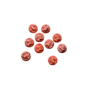 May include: A collection of 10 small, round, coral-colored buttons with a floral design. The buttons are scattered on a white background.