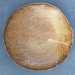 Può includere: Una ciotola in ceramica marrone con un motivo a spirale di linee. La ciotola ha una finitura lucida ed è fatta a mano.