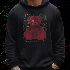 May include: Black hoodie with a red teddy bear graphic. The bear has one eye closed and a purple X over its other eye. The background of the graphic is a green and red splatter pattern.
