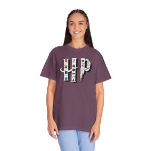 May include: A mauve-colored t-shirt featuring the letters "HP" in a stylized design. The letters are filled with various small illustrations. The shirt has short sleeves and a relaxed fit.