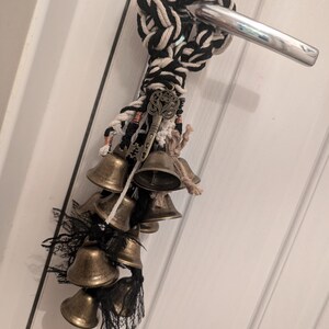 May include: A black and white rope door knocker with a key charm and a cluster of brass bells hanging from it.