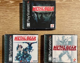 May include: Three PlayStation game cases for Metal Gear Solid. The cases feature the game's title in red and white, with various action-oriented graphics and the PlayStation logo. The cases are in clear plastic.