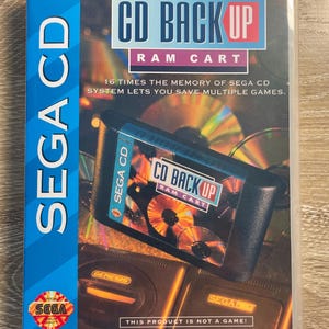 May include: A SEGA CD game cartridge labeled "CD BACK UP RAM CART" in a clear plastic case. The cartridge is black with blue and red text. The packaging includes the SEGA logo and text: "Pick Up Where You Left Off In Your Favorite Games!"