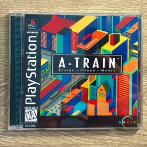 May include: A PlayStation game case for "A-Train." The cover art shows a vibrant cityscape with the game's title and the words "Trains, Power, Money." The case is in a clear plastic jewel case.