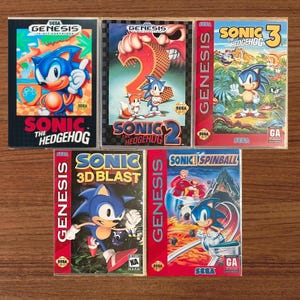 May include: Five Sega Genesis video game cases featuring Sonic the Hedgehog titles: Sonic the Hedgehog, Sonic the Hedgehog 2, Sonic the Hedgehog 3, Sonic 3D Blast, and Sonic Spinball. Each case displays colourful character artwork and game logos.