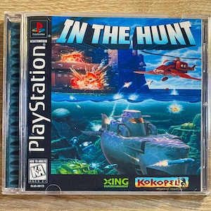 May include: A PlayStation game case for "In The Hunt." The cover art shows a submarine, explosions, and a red helicopter above water. The game title is in large, blue letters. The case is in a clear plastic case.