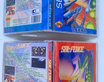 May include: Two Sega CD game cases for the game Sol-Feace. The cases are blue and red with a picture of a spaceship and a dragon on the front. The back of the cases have text describing the game.
