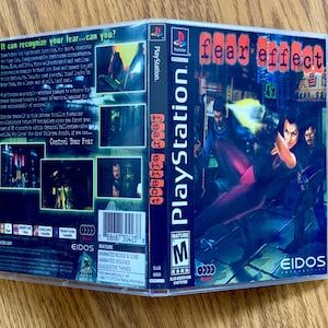 Può includere: Una custodia per giochi PlayStation per "Fear Effect" con un'immagine in bianco e nero di una donna che tiene una pistola e un uomo sullo sfondo. La custodia è etichettata "Mature" e ha una classificazione "M" per pubblico adulto. Il retro della custodia contiene una descrizione del gioco e un elenco di avvertenze sul contenuto, tra cui sangue e viscere animate, violenza animata e temi suggestivi.