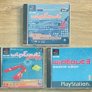 May include: Three PlayStation game cases from the "Wipeout" series. The cases have blue, red, and yellow graphics. The top case has Japanese text. The bottom right case says "Wipeout 3 Special Edition".