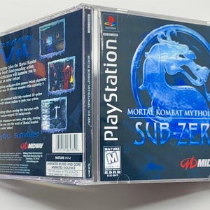 Puede incluir: Caja de juego de PlayStation para "Mortal Kombat Mythologies: Sub-Zero". La portada presenta un diseño de dragón azul y el título del juego. La parte posterior de la caja tiene capturas de pantalla y texto. El juego está clasificado como Mature.