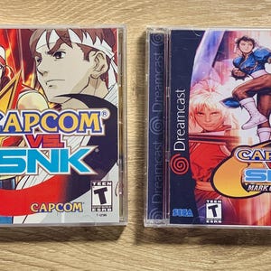 May include: Two Dreamcast video game cases. The first case is for Capcom vs SNK. The second case is for Capcom vs SNK 2: Mark of the Millennium 2001.