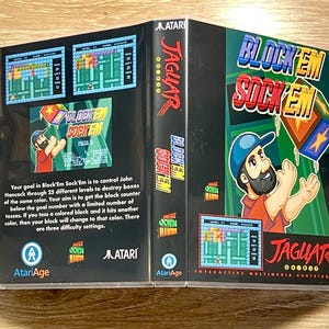 May include: A Block'Em Sock'Em video game cartridge for the Atari Jaguar. The box art features a cartoon man in a blue hat, the game's title, and gameplay screenshots. The game's description is also visible on the back of the box.