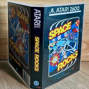 May include: A clear plastic game case for the Atari 2600 video game Space Rocks. The cover features a blue background with a white spaceship, a red flying saucer, and yellow text reading Space Rocks. The spine displays Atari 2600 and Space Rocks.