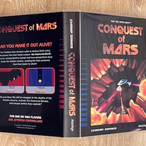 May include: A retro video game case for "Conquest of Mars" for the Atari 2600. The cover features a spaceship firing lasers in a red and orange space scene. The back includes game screenshots and text: "Can you make it out alive?"