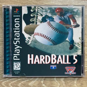 Puede incluir: Caja de juego de PlayStation para Hardball 5. La portada presenta una pelota de béisbol, un bateador y el título del juego en blanco y rojo. La caja está en una caja de plástico transparente.