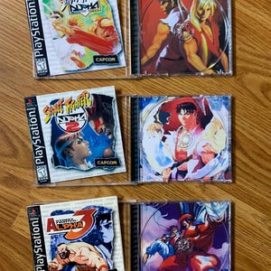 Op de afbeelding: Drie PlayStation-videogame-hoezen voor Street Fighter Alpha-games. De hoezen zijn in een rij van links naar rechts gerangschikt, waarbij de eerste hoes Street Fighter Alpha 1, de tweede hoes Street Fighter Alpha 2 en de derde hoes Street Fighter Alpha 3 laat zien.