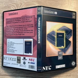 May include: A black Turbo EverDrive box with the TurboGrafx logo and product information. The box features images of the EverDrive and a TurboGrafx-16 console. Text on the box describes the product's features and functionality.