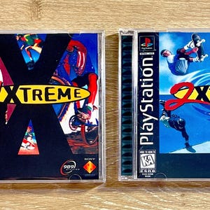 May include: Two PlayStation video game cases. The first, "1 XTREME," features a black background with action sports figures and the game title in yellow and red. The second, "2 XTREME," has a blue background with similar graphics.