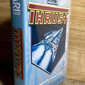 May include: A clear plastic game case for the Atari 2600 video game titled Thrust+. The cover features a spaceship flying through space, the text XYPE, and the words Programmed by Thomas Jentzsch and Platinum Edition printed on a light blue background.