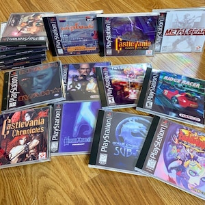 May include: A collection of 14 PlayStation video game cases, featuring titles such as "Castlevania: Symphony of the Night", "Ridge Racer", "Metal Gear", "Mortal Kombat 3", "Ivan "Ironman" Ivanovich", "Wipeout", and "Street Fighter Alpha 2".