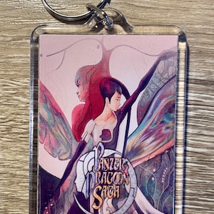 May include: A clear acrylic keychain with a colorful image of two figures with wings. The image has a pink background and the text "Panzer Dragoon Saga" in gold lettering.