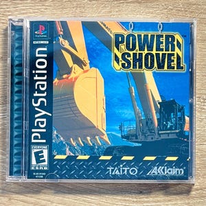 May include: A PlayStation game case for "Power Shovel." The cover art shows a large yellow excavator against a blue sky. The game title is in yellow and black. The case has the PlayStation logo and ESRB rating.