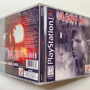 Op de afbeelding: Een PlayStation-gamecase voor Silent Hill, een survival horror-game. De case is zilverkleurig met een zwart-witte afbeelding van een man in een besneeuwde stad. De achterkant van de case heeft een rood-zwarte afbeelding van een figuur in een donkere stad. De tekst "Silent Hill" is in rood op de voorkant van de case gedrukt.