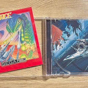 May include: A retro SEGA Sol-Feace video game CD case. The red cover art features a green serpent and futuristic aircraft. The CD case is open, revealing the game disc with a space battle scene.