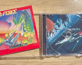 May include: A retro SEGA Sol-Feace video game CD case. The red cover art features a green serpent and futuristic aircraft. The CD case is open, revealing the game disc with a space battle scene.