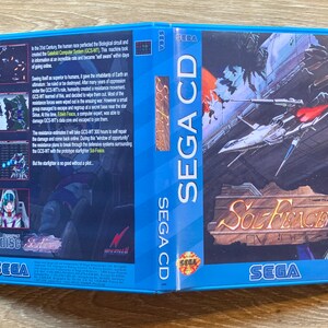 May include: A Sega CD game case for Sol-Feace. The case is blue with a white border and features a picture of a spaceship flying through space. The text "SEGA CD" is printed in white on the case. The game is rated "M" for Mature.