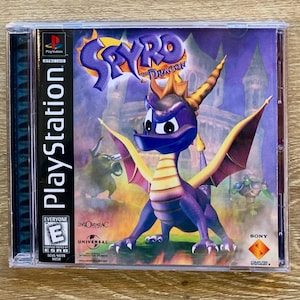 Op de afbeelding: Een paarse en gele PlayStation-gamecase van Spyro the Dragon met een paarse draak op de voorkant. De game is door de ESRB met E voor iedereen beoordeeld.