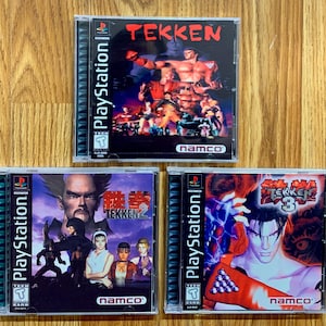 Puede incluir: Tres cajas de juegos de PlayStation para Tekken 1, Tekken 2 y Tekken 3. Las cajas son todas negras con un logotipo de PlayStation azul y un logotipo de clasificación "TEEN" rojo, blanco y azul. Los juegos están hechos por Namco.