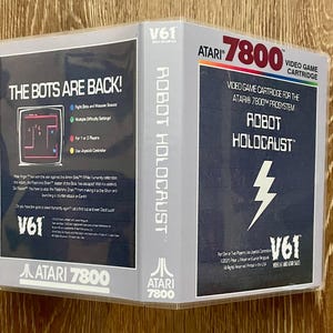 May include: A vintage Atari 7800 video game cartridge for Robot Holocaust. The game box features the title in bold white letters with a lightning bolt graphic on a dark blue background. The back of the box has the text "The Bots Are Back!"