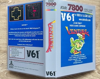 May include: Atari 7800 Venture video game cartridge case with blue and light gray panels. The front features the Venture logo, a green dragon illustration, and text including V61 Video 61 & Atari Sales. The back displays game screenshots.