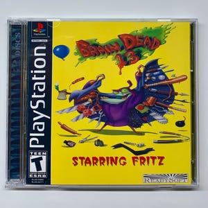 May include: Brain Dead 13 PlayStation game case. The yellow cover features a cartoon character with various objects, including a baseball bat and a chainsaw. The game title is in red, with the text "Starring Fritz" below. The PlayStation logo is on the side.