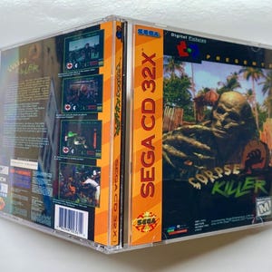 May include: A Sega CD 32X game case with a bright orange spine and a black and white image of a zombie on the front. The game is called "Corpse Killer" and is presented by Digital Pictures.